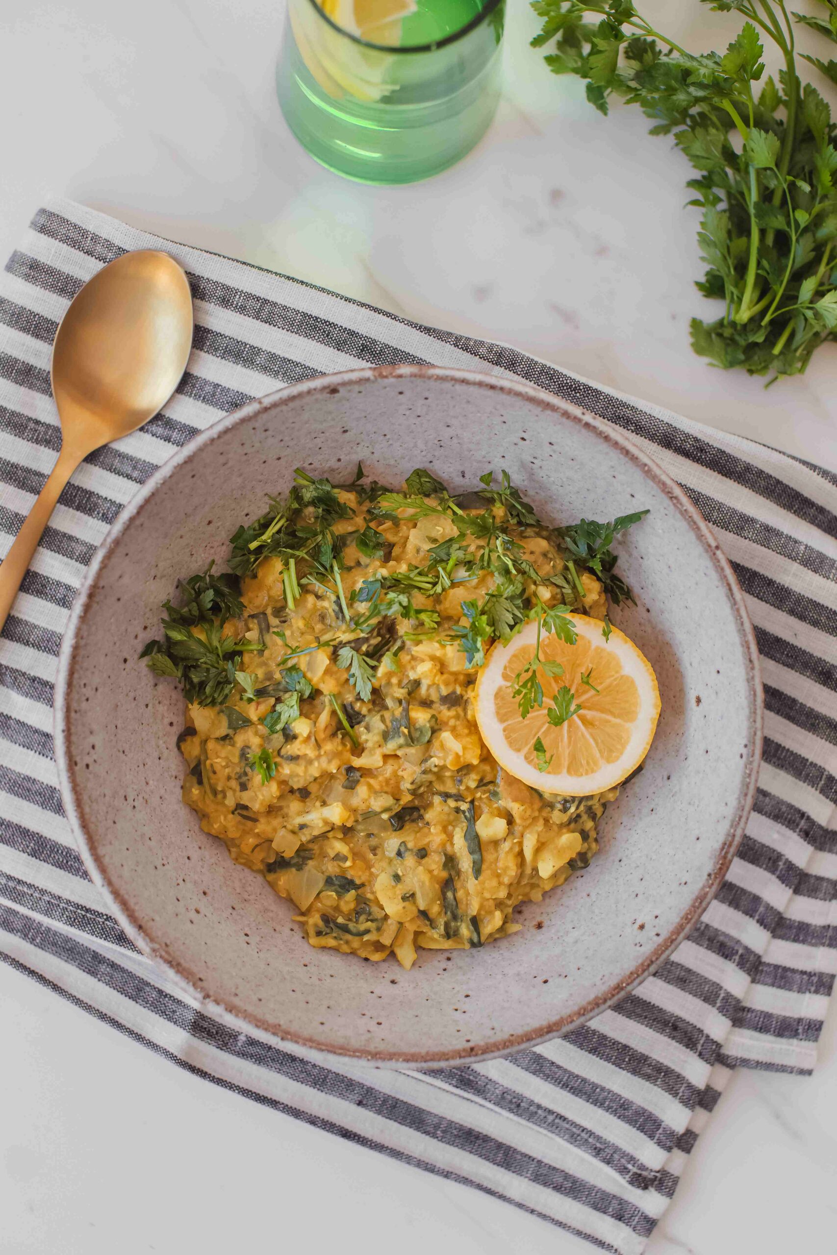 Hero image of a comforting bowl of spinach and cauliflower dahl on a marble bench top with a navy stripe tea towel in the background.